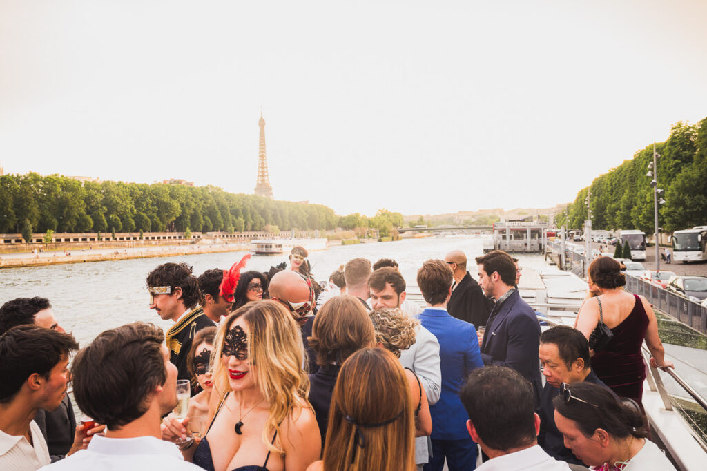 Croisière de gala AIME 2026 sur la Seine : invités sur le pont du bateau au coucher du soleil, tour Eiffel au loin