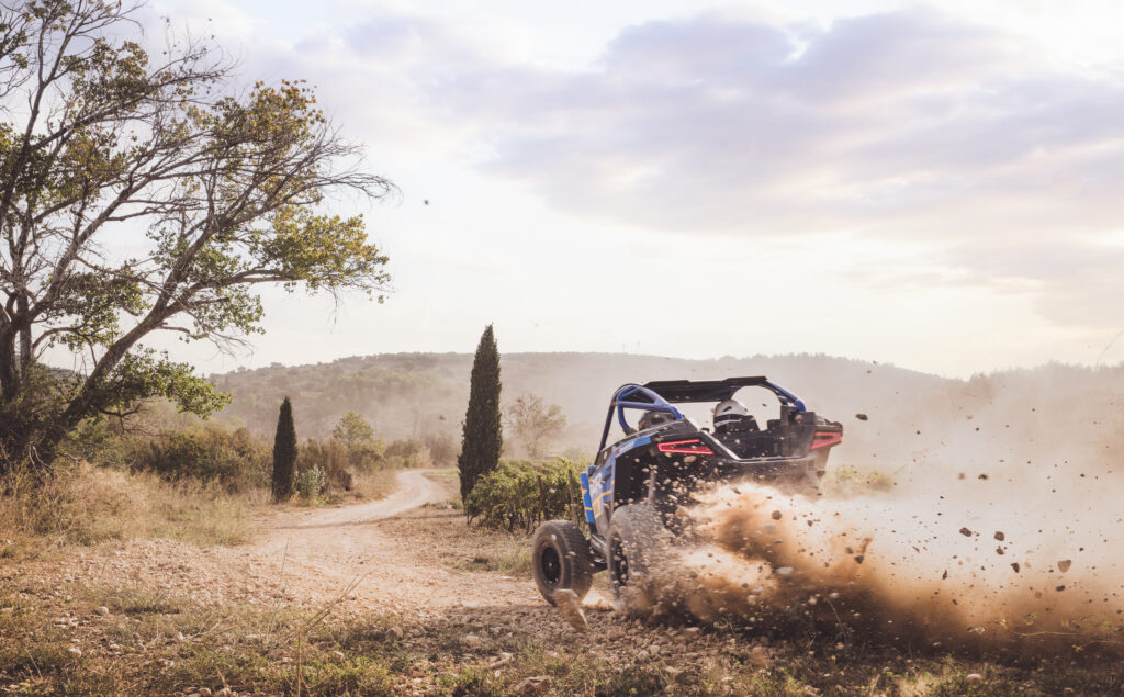 Buggy bleu dans un virage sur piste de terre, nuage de poussière, reportage BF Goodrich