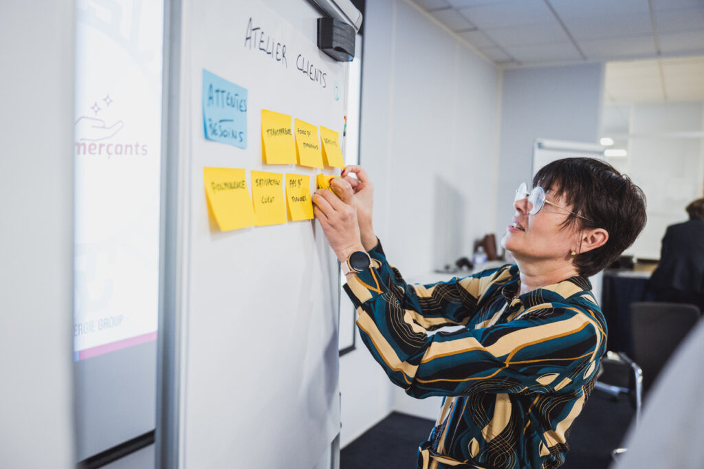 OMS Synergie : participante qui colle un post-it sur un mur d’idées